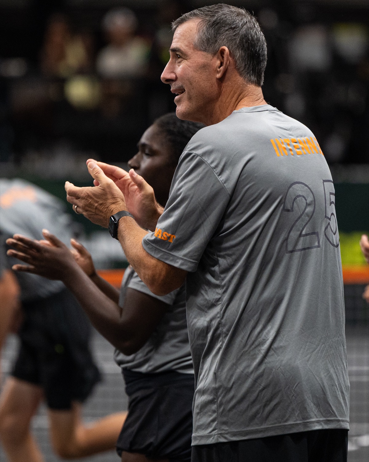 A guest coach in a grey Challenge shirt applauding courtside alongside a player.