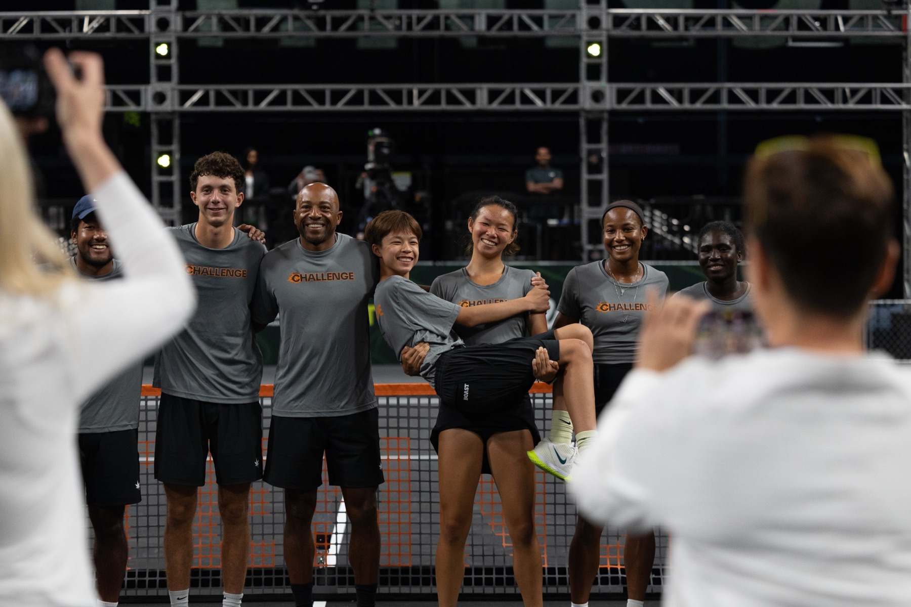 The Challenge Team posing together at the net in grey Challenge shirts, one player being carried by teammates.